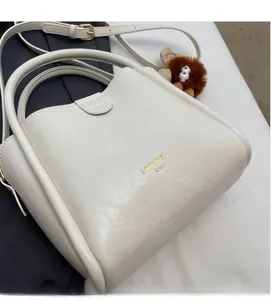 Detail view of cream leather handbag with litchi texture and cute plush bear charm