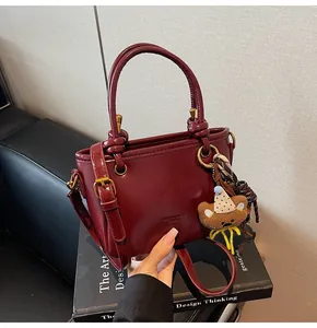 Dettaglio borsa rosso scuro in pelle cerata con ciondolo a forma di orso e sciarpa