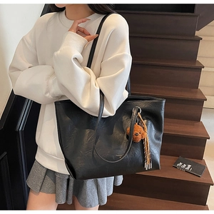 Black leather tote bag with a cute brown plush bear charm shown in a lifestyle setting
