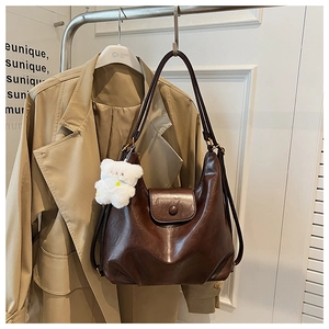 Détail d'un sac bandoulière en similicuir marron avec breloque ours en peluche et boucle