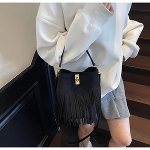 Detail showing the black tassel bucket bag with a gold twist lock and matte suede finish