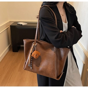 Detail of vintage brown tote bag with cute plush puppy charm and woven tassel accent