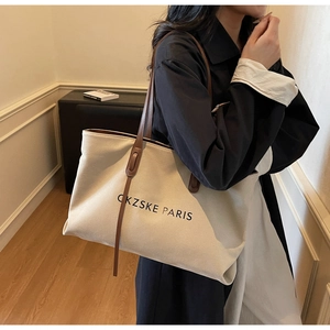 Vue détaillée du sac cabas en toile crème avec finitions et bandoulière en cuir marron