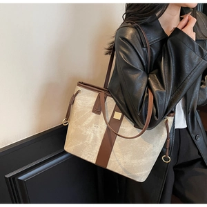 Vue détaillée du grand sac cabas beige avec finitions en cuir marron porté sur une veste noire