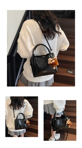 Detail of black pebbled leather tote with gold branding and cute plush bear charm