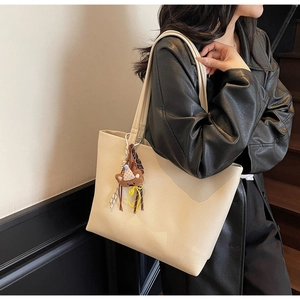 Close-up of minimalist cream tote bag with litchi texture and a cute bear charm on shoulder