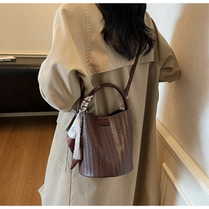 Détail d'un sac seau tressé marron avec foulard en soie et poignée ronde rigide