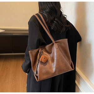 Detail of a large brown leather tote bag with a cute puppy charm shown on a model's shoulder