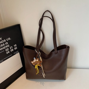 Close-up of dark brown lychee grain leather tote bag with a cute striped bear charm