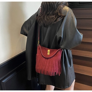 Close-up of deep red suede bohemian fringe bag with gold metal clasp on shoulder