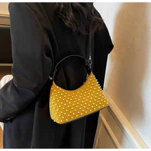 Detailed view of a yellow studded shoulder bag with pearls and silver hardware on a model