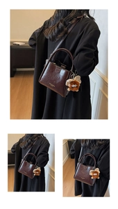 Detail of dark brown leather handbag featuring a plush charm and gold brand logo