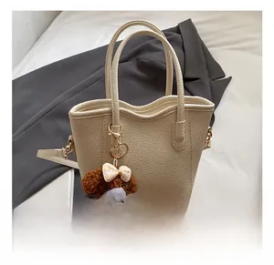 Detail der cremeweißen Beuteltasche mit Narbenleder und süßem braunem Bärenanhänger