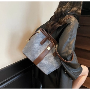 Détail du sac seau en denim bleu avec garniture en cuir brun et logo métallique