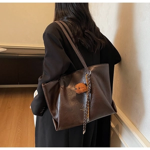 Detail of a dark brown faux leather tote bag with plush dog charm and woven rope detail