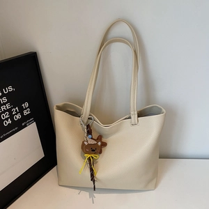 Close-up of cream leather tote bag with lychee texture and cute bear charm pendant