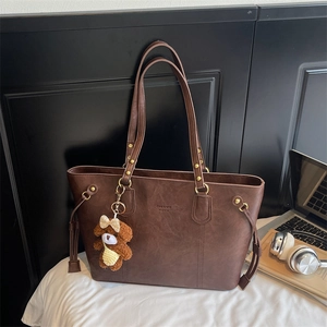 Détail d'un sac cabas en similicuir marron avec logo et breloque ours en peluche