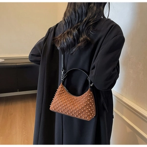 Brown beaded hobo shoulder bag with a crescent shape worn over a black winter coat