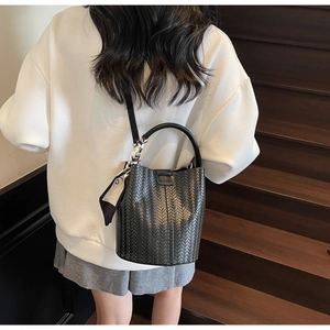 Détail du sac seau noir tressé avec étiquette de mode et décoration de foulard en soie