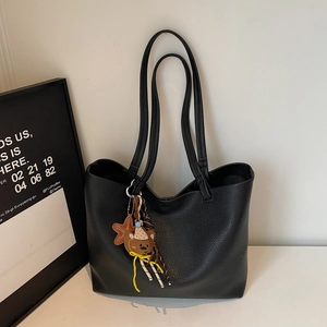 Detail of minimalist black leather tote bag featuring a cute teddy bear and star charm hanger