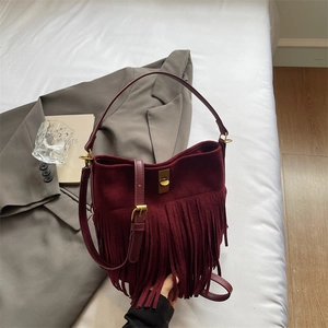 Detail of burgundy suede fringe bucket bag featuring golden twist lock on white bedding