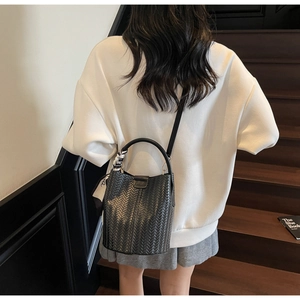 Détail du sac seau tressé noir avec foulard en soie et boucle métallique ronde à logo