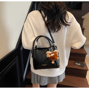 Detail of black lychee grain leather handbag featuring a plush monster charm on the side