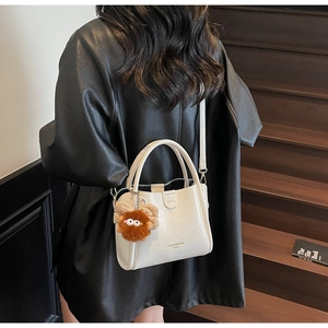 Detail showing white lychee pattern leather handbag with brown plush monster charm and strap
