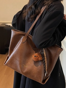 Brown leather tote bag with teddy bear charm shown on model in a cozy interior setting