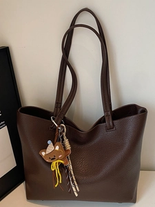 Minimalist coffee brown faux leather tote bag with a cute bear charm on a white desk