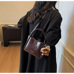 Detailed view of brown litchi leather handbag with cute monster charm and gold logo