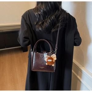 Detail of reddish-brown lychee textured leather bag with gold logo and plush charm