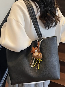 Black textured leather tote bag with cute bear charm worn on shoulder in a lifestyle setting
