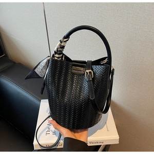 Détail d'un sac seau tressé noir avec foulard en soie et poignée ronde rigide