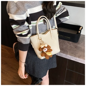 Detail der cremeweißen Mini-Tasche mit süßem braunem Teddybär-Anhänger am Schultergurt