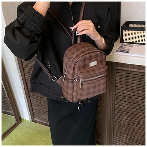 Detail of a brown checkered backpack with silver metal plate and dual zipper texture