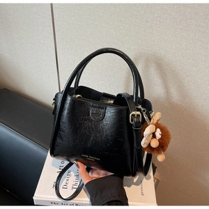 Detail of black lychee texture leather handbag with golden logo and cute plush monster charm