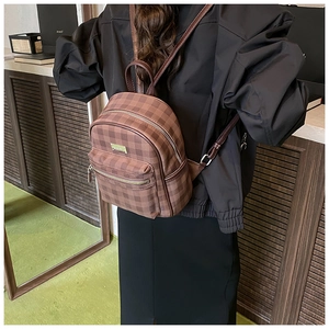 Brown checkered mini backpack with silver zipper and front pocket shown on a model