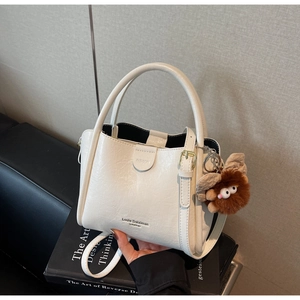 Close-up of cream leather tote bag with lychee texture and soft brown pompom charm