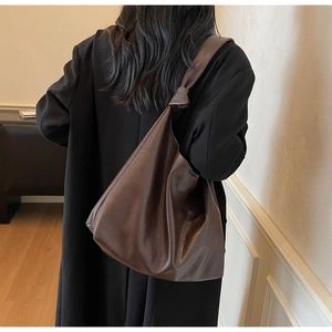 Détail du sac hobo en cuir souple marron foncé avec un nœud décoratif sur la bandoulière