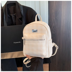 Detail of beige checkered small backpack showing front zip pocket and metal logo plate