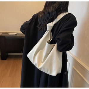 Détail du grand sac cabas crème avec bandoulière nouée porté sur un manteau noir