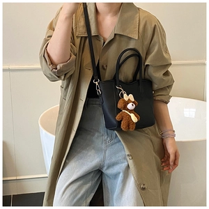 Detail der schwarzen Leder-Beuteltasche mit süßem Bärenanhänger zum beigen Trenchcoat
