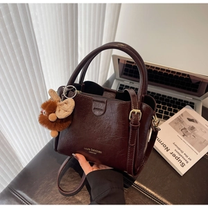 Detailed view of dark brown pebbled leather handbag with plush charm and office props