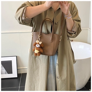 Detailansicht der braunen Eimer-Tasche mit Ledermaerung und süßem Teddybär-Anhänger