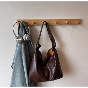 Détail du sac hobo en cuir marron foncé avec bandoulière nouée et texture souple