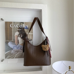 Détail du sac à bandoulière tressé marron foncé avec breloque ours et écharpe rayée