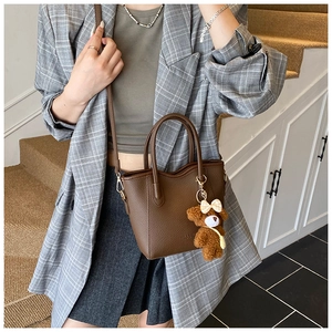 Detail einer dunkelbraunen Handtasche aus Leder mit Plüschbären-Anhänger und Schultergurt