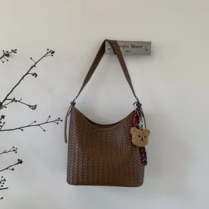 Détail du sac seau marron tressé à la main avec breloque ours en peluche et ruban rayé