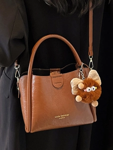Brown litchi pattern leather handbag with plush charm shown on person